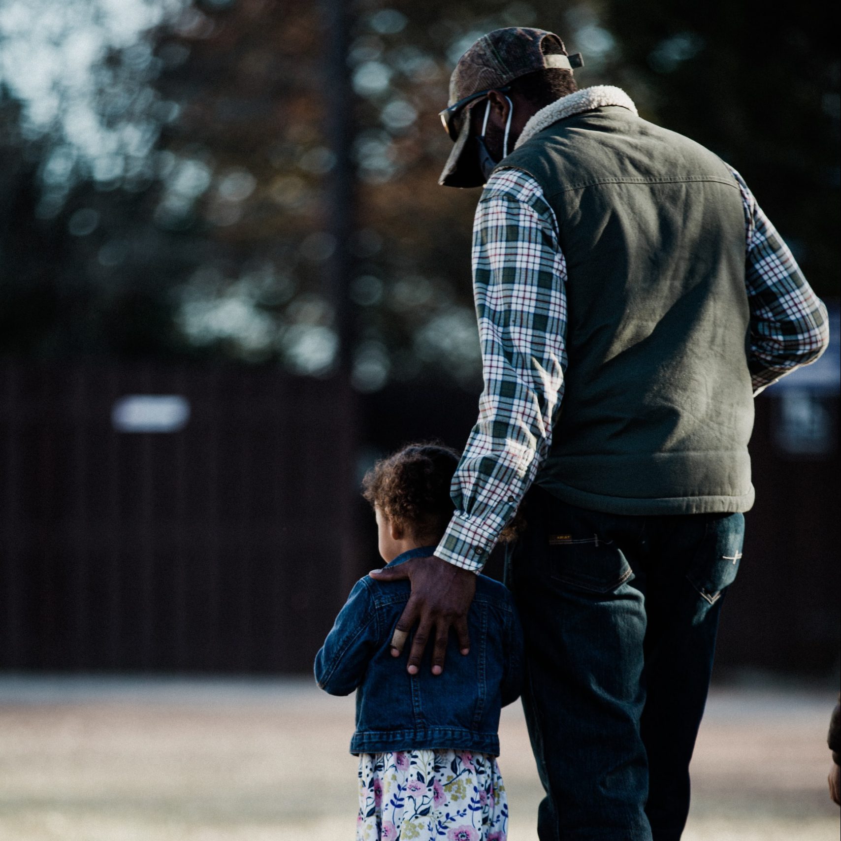 Adult walking outdoors with a child, a hand resting supportively on the child's back